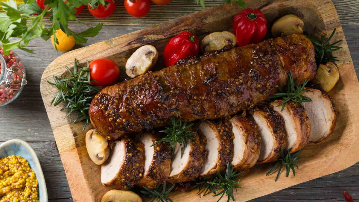 Polędwica w sosie – przepisy na karnawałowe danie w „Pytaniu na śniadanie”. Na drewnianej desce ułożona jest pieczona polędwica pokrojona w plastry, posypana ziołami i ziarnami musztardy. Danie podane jest z pieczarkami, papryką, pomidorami koktajlowymi oraz gałązkami rozmarynu.